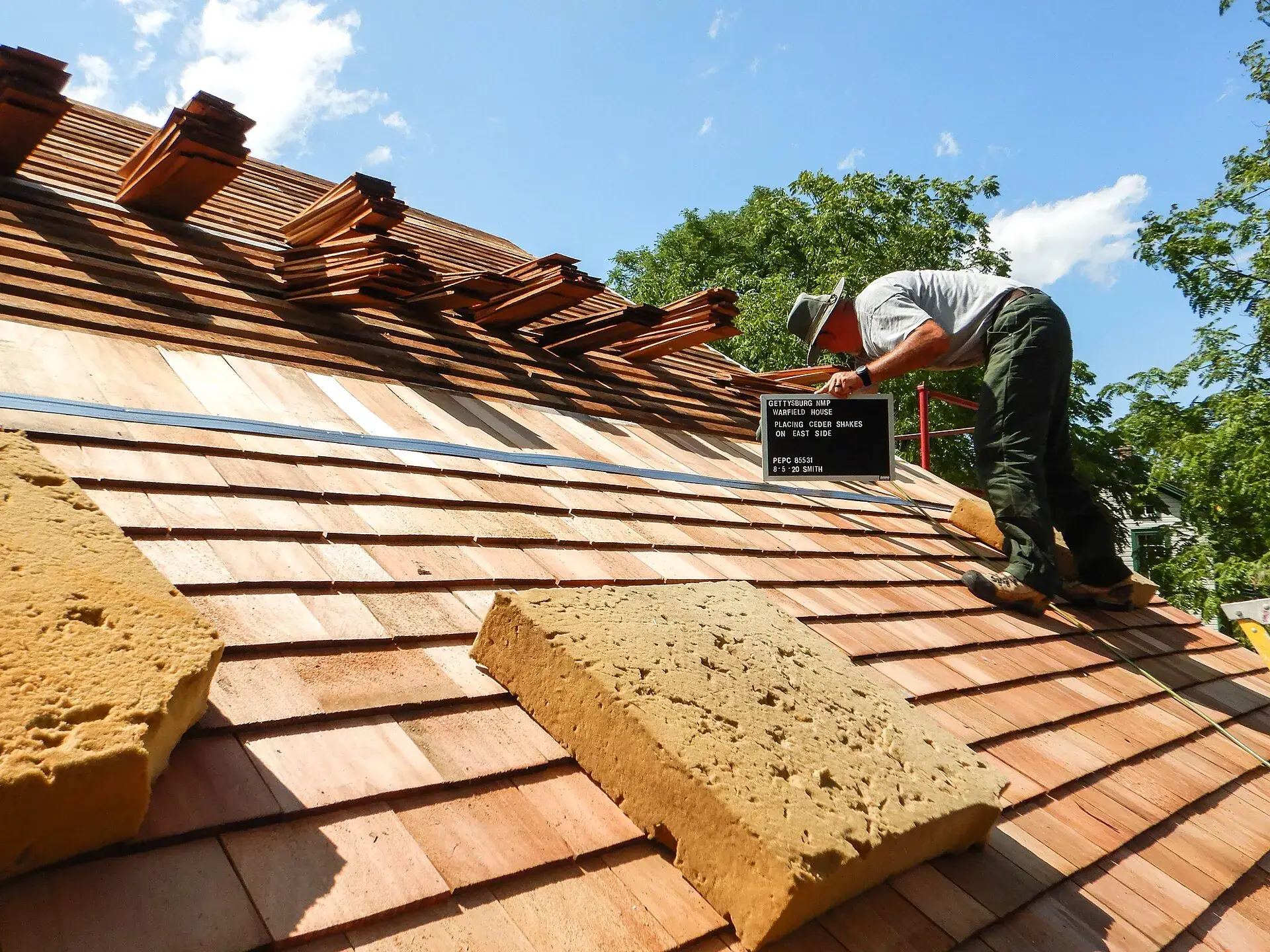 A roofer laying cedar shakes on a steeply pitched roof